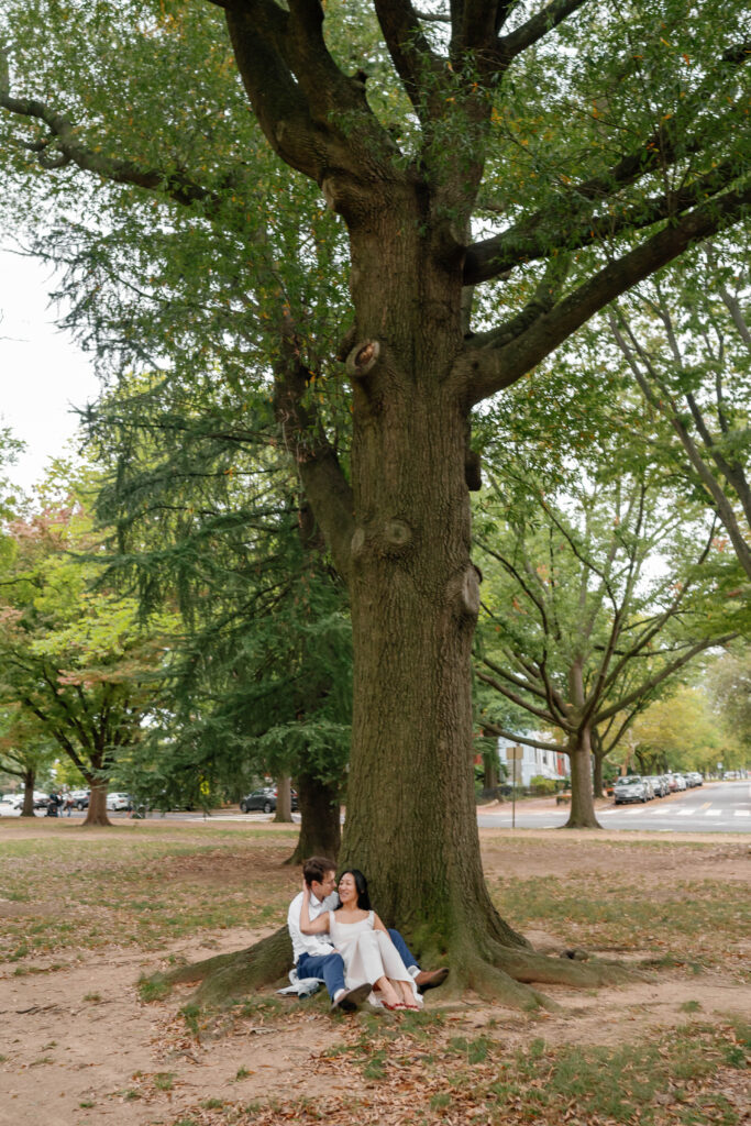 Couple sitting under large tree in Capitol Hill park during Washington DC engagement session
