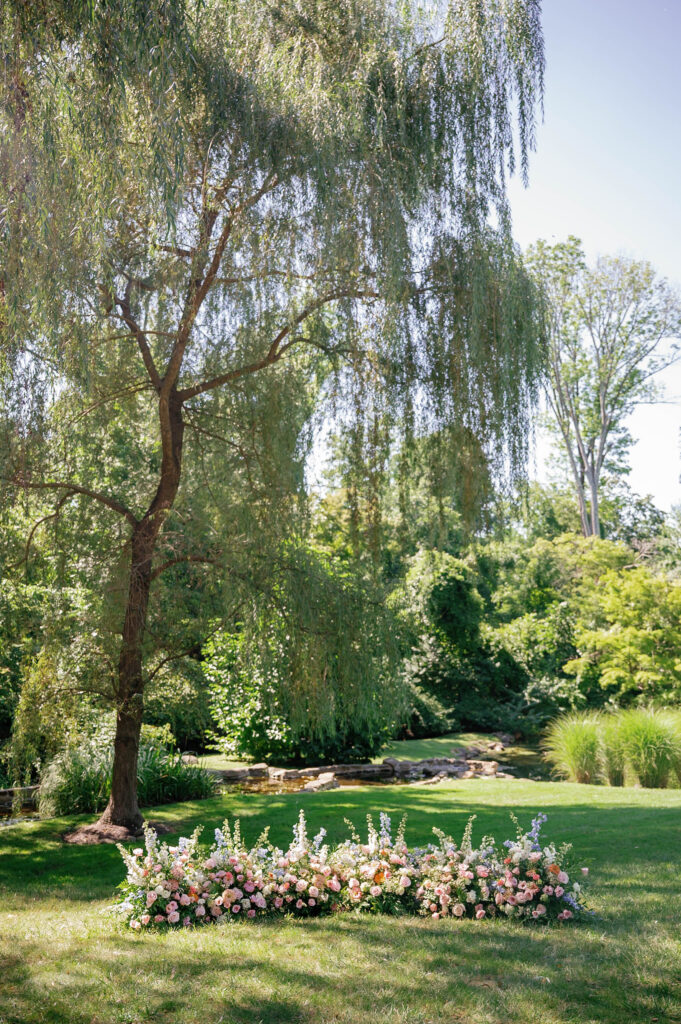 Ceremony space at Appleford Estate featuring lush greenery, willow trees, and romantic floral arrangements creating a peaceful garden setting for the wedding celebration.
