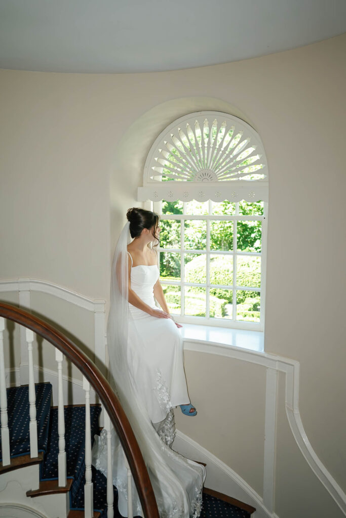 Bride sitting in the curved staircase window inside the historic Appleford Estate manor house during indoor wedding portraits.
