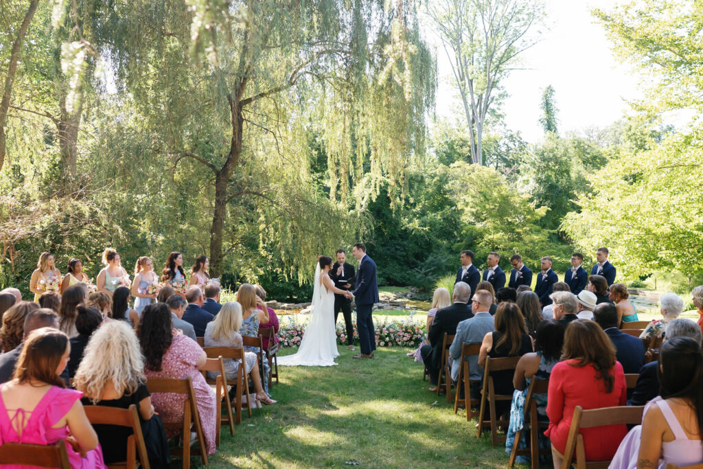 Christian and Emily exchanging vows during their outdoor garden ceremony at Appleford Estate surrounded by family and friends on a warm summer afternoon.
