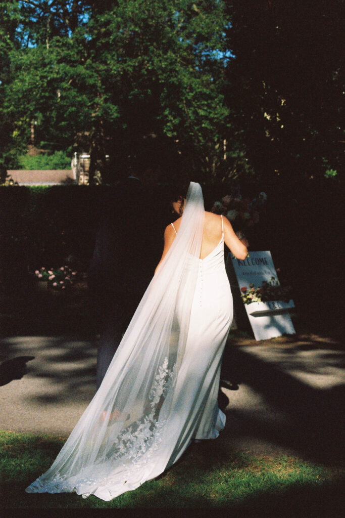 Bride walking through the gardens at Appleford Estate with her veil flowing behind her during the evening celebration.